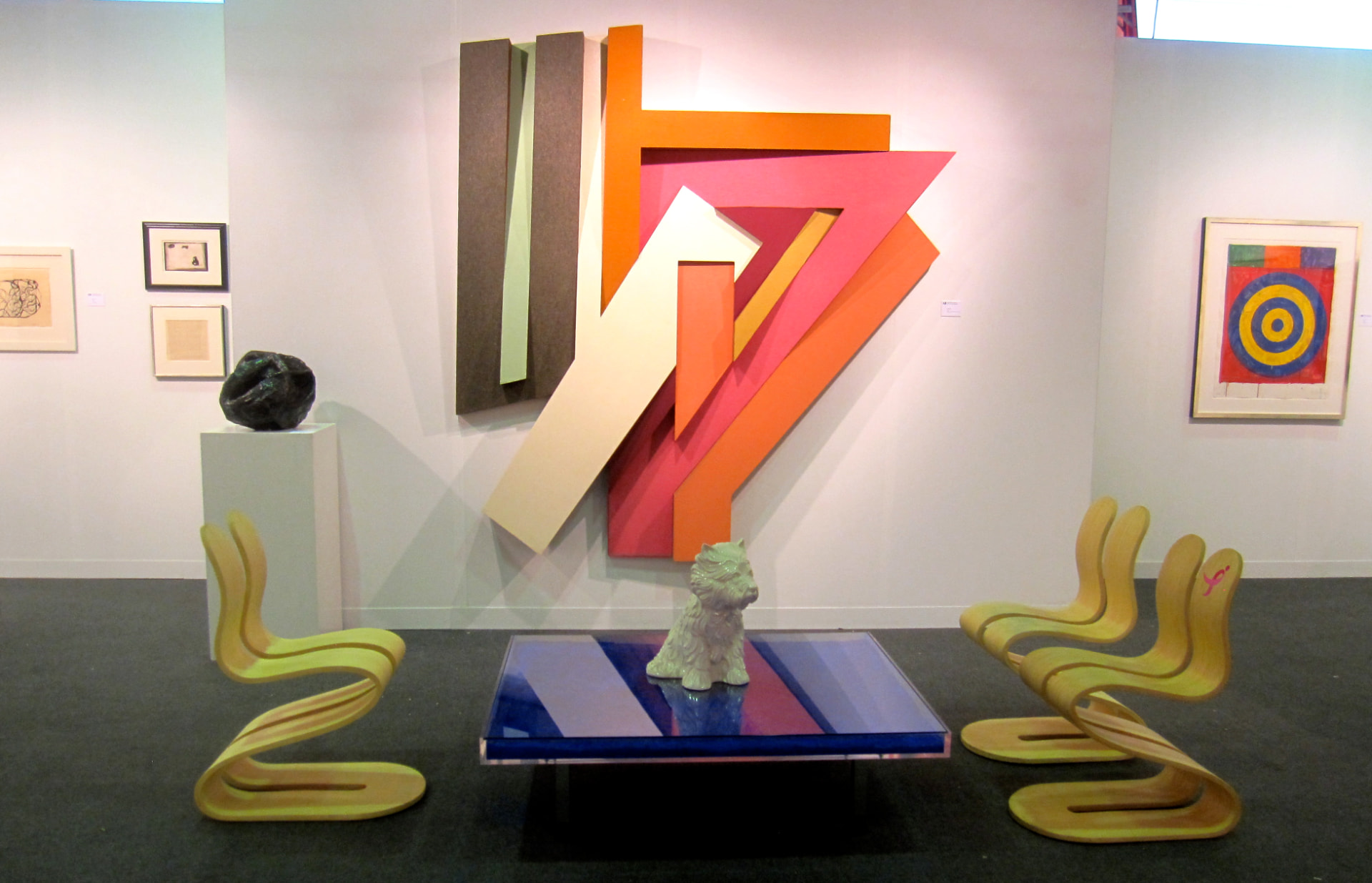 Art fair booth with two bamboo Fluid Ribbon Chairs flanking a coloured relief work